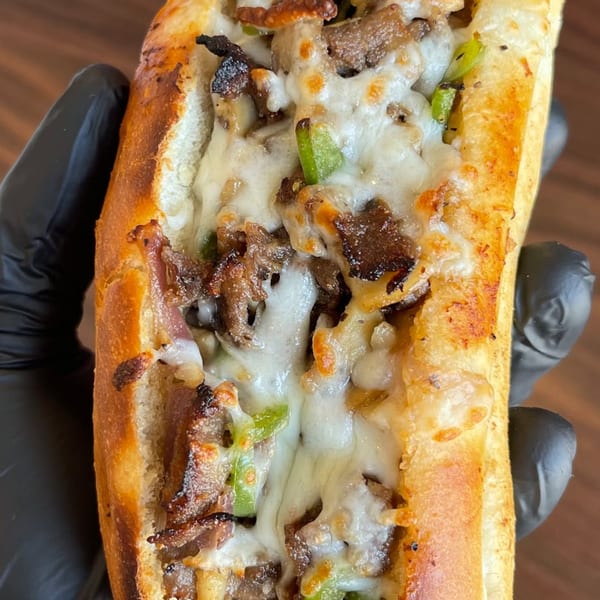 A close-up of a cheesesteak sandwich with melted cheese, steak, and green peppers.