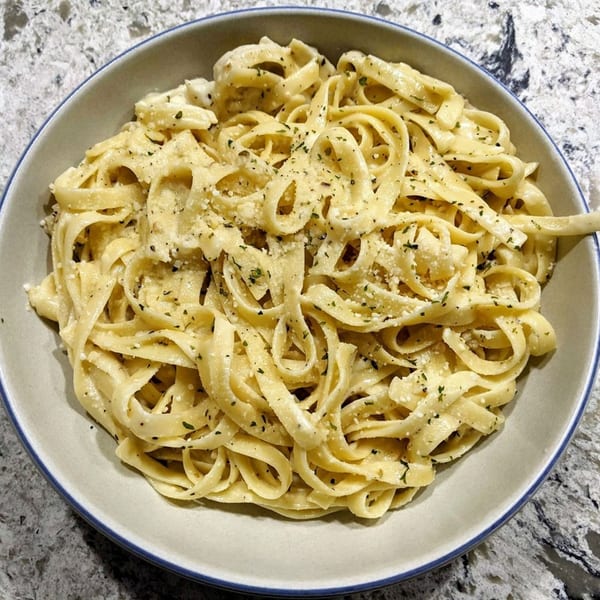 A bowl of creamy fettuccine alfredo pasta, topped with herbs and parmesan cheese.