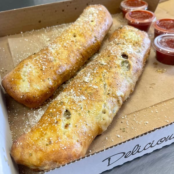Two golden-brown calzones, dusted with parmesan cheese, in a Pizza Nation box with marinara dipping cups.