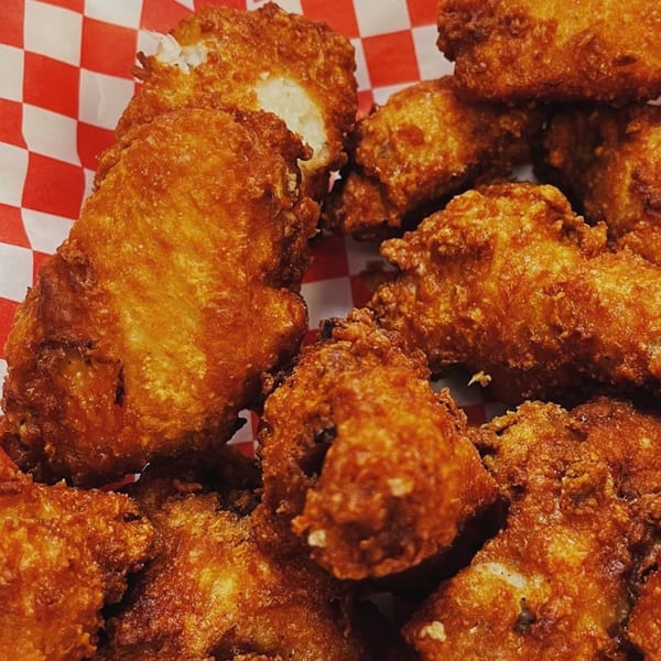 Close-up of golden-brown fried cheese curds in a red and white checkered paper basket.