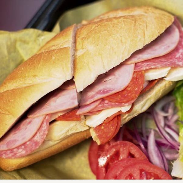 A large deli sub sandwich with ham, salami, cheese, tomatoes, and red onions.
