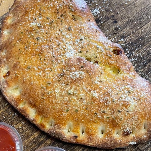 Golden-brown calzone from Pizza Nation, sprinkled with herbs and parmesan, on a wooden surface.